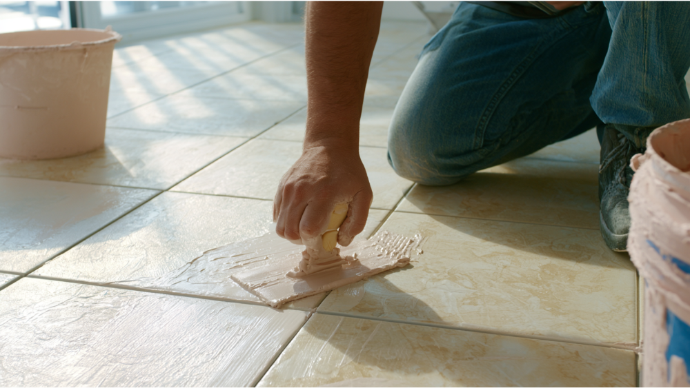 Applying fresh grout between ceramic floor tiles using a rubber grout float.