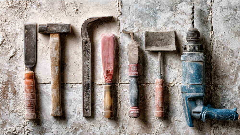 Collection of tile removal tools including grout saw, cold chisel, hammer, pry bar, floor scraper, and rotary hammer.