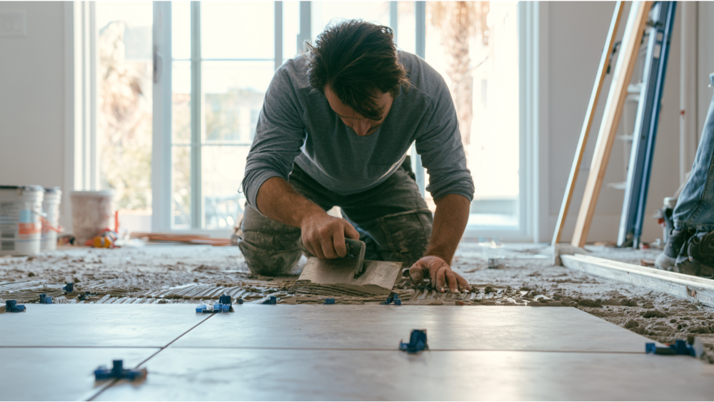 Professional tile installer laying large porcelain floor tiles with thinset mortar, spacers, and leveling clips during a residential tile installation project.