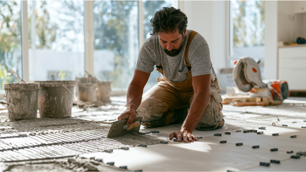 Professional installer laying porcelain floor tiles with thinset mortar and leveling clips on a prepared subfloor.