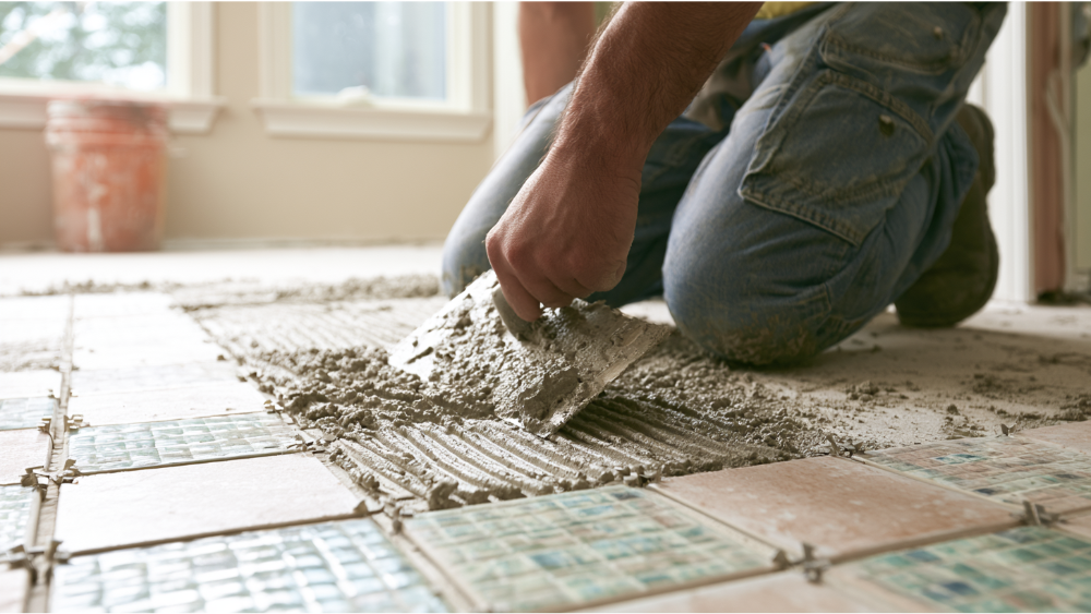 Professional installer applying modified thinset mortar over prepared ceramic floor tiles before laying new porcelain tile.