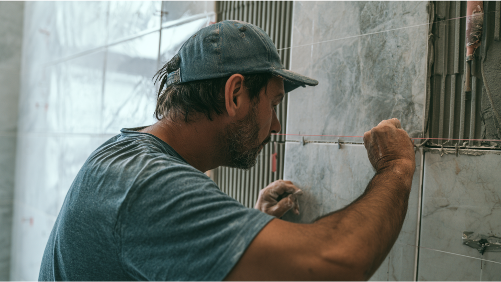 Experienced tile contractor installing large-format bathroom wall tiles with precision tools during a professional residential remodeling project.